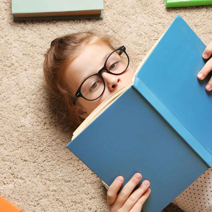 Alfombra residencial color neutro con niña con lentes recostado leyendo un libro