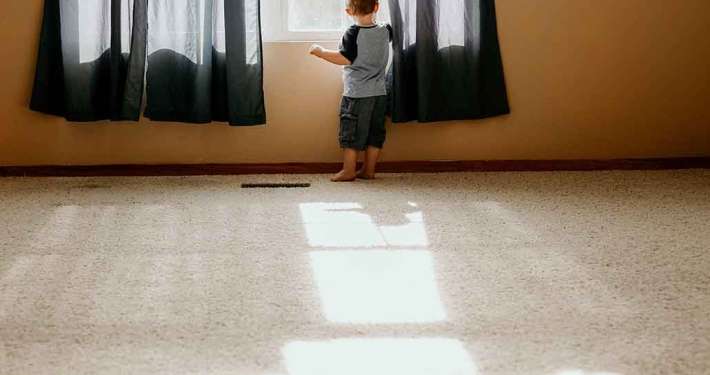 Niño descalzo sobre una alfombra residencial en color claro asomado en una ventana