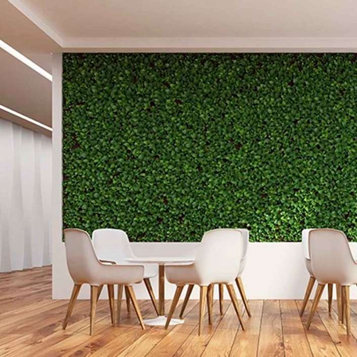 Muro verde artificial interior en pared de comedor con mesas y sillas blancas con base de madera