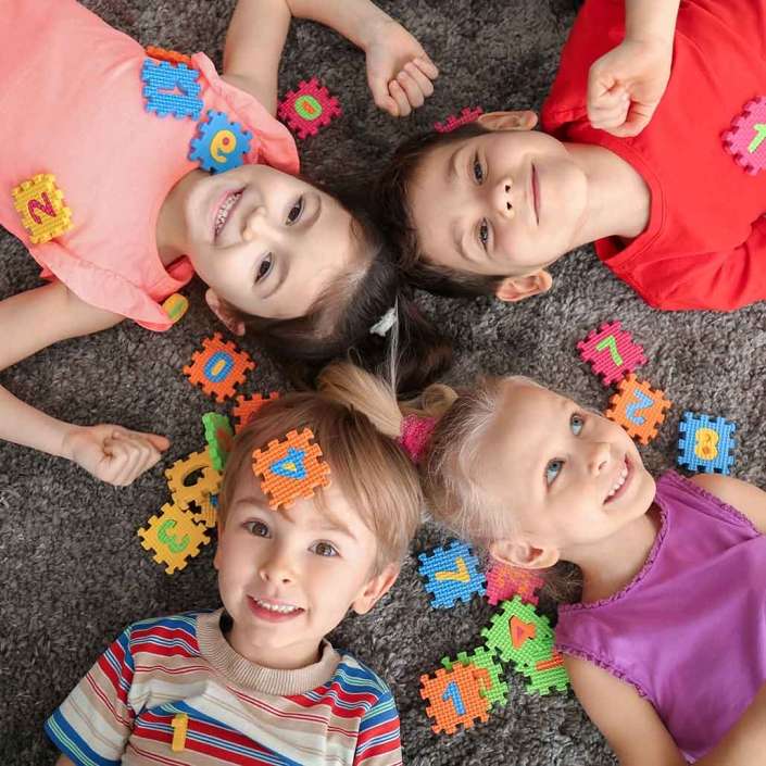 Niños sonriendo recostados sobre una alfombra color gris