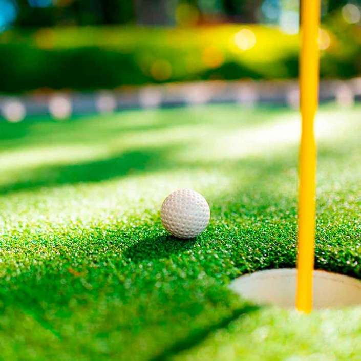 Pasto sintético deportivo en campo de golf con close up de pelota de golf muy cerca de entrar en un hoyo del campo
